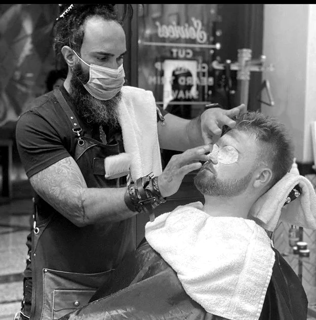 Reza giving a client a hot towel face treatment in the barber chair